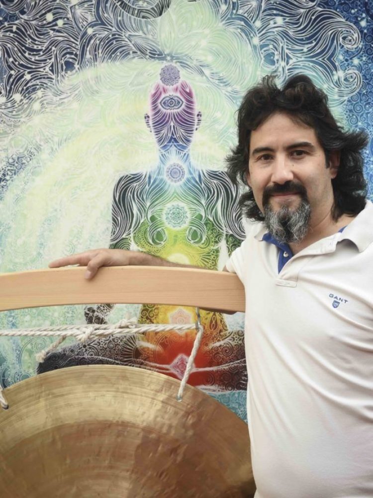 photo de Dominique avec son fen gong et toile de décor avec la silhouette d'une personne méditant avec les chakras